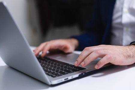 Close-up of male hands typing on laptop at desk in officeの写真素材