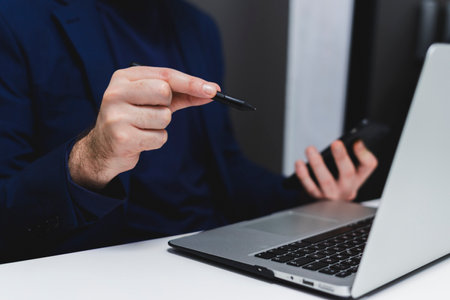 cropped view of businessman working with laptop and holding pen in officeの写真素材