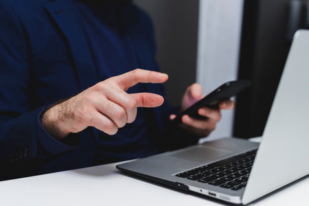 Close-up of male hands using mobile phone and laptop in officeの写真素材