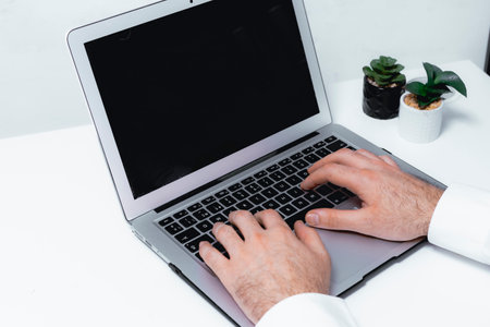 cropped view of businessman typing on laptop with blank screen in officeの写真素材