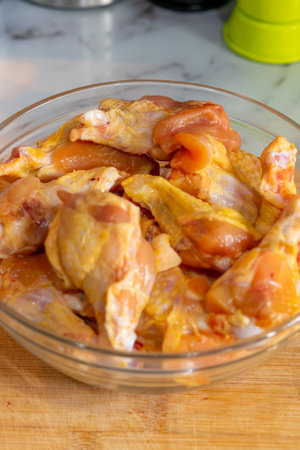 Raw chicken pieces in a glass bowl on a wooden cutting board.の写真素材