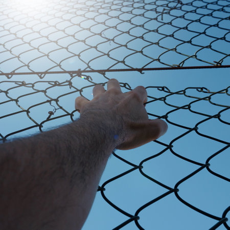 man hand grabbing metallic fence, feeling freeの写真素材