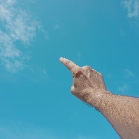 Man's hand pointing on blue sky background with copy space for textの写真素材