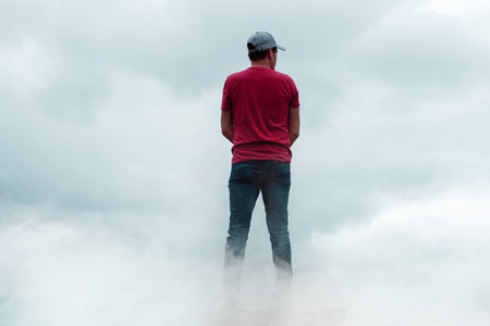 Man standing on the top of the mountain and looking at the clouds