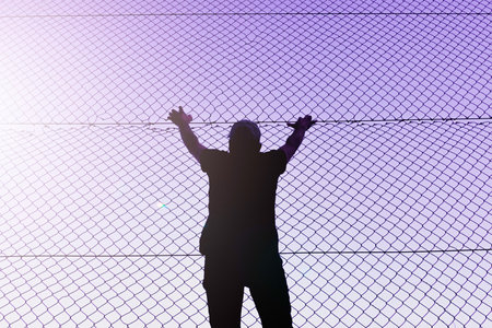 Silhouette of a woman standing in front of a fence.