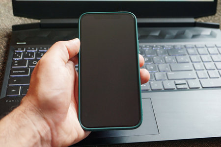 Smartphone with blank screen in hand on the background of a laptopの写真素材