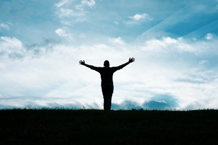 Silhouette of a man with open arms on blue sky backgroundの写真素材