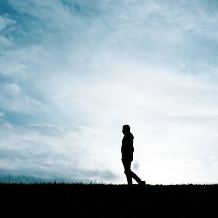 Silhouette of a man walking on the grass with sky background