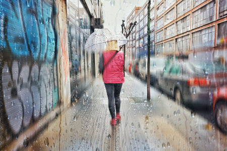 Rainy day in the city. A young woman is walking along the street.の写真素材
