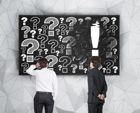 two businessman looking at exclamation and question markの写真素材