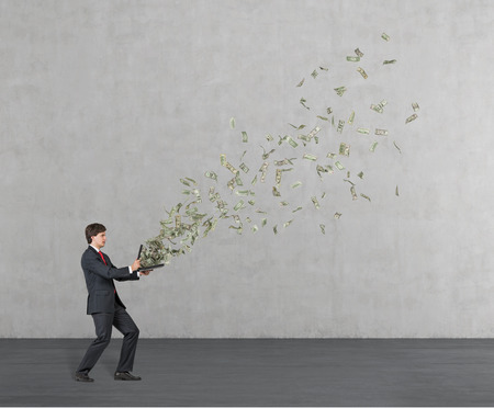 businessman holding briefcase from which fly out dollarsの写真素材