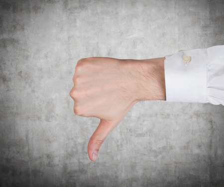 hand showing thumb down on a gray background