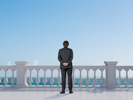 businessman standing on balcony and looking to oceanの写真素材
