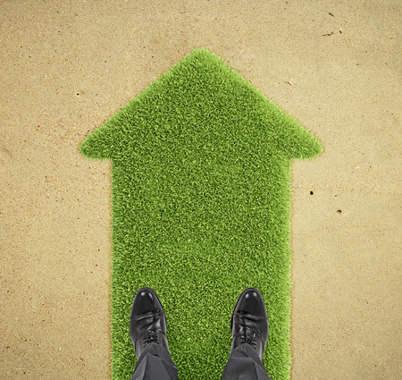 businessman standing on big green grass arrowの写真素材