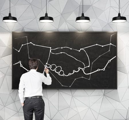 businessman drawing handshake symbol on chalk boardの写真素材