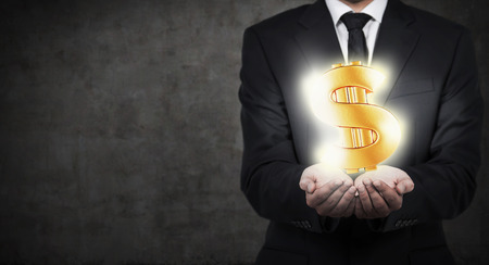 businessman holding gold dollar symbol isolation on grayの写真素材