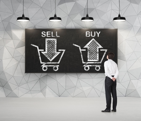 Businessman is thinking about the choice 'sell or buy', arrows on the blackboard. A concept of the trader who is forming a portfolio by selling and buying assets.の写真素材