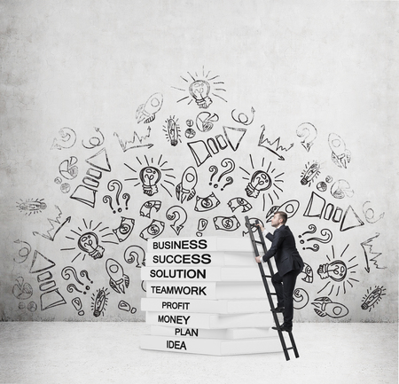 A businessman is climbing up to the knowledge. A ladder and a book's pedestalの写真素材