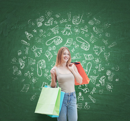 A happy young woman with the colourful shopping bags from the fancy shops. Shopping icons are drawn on the green wall.の写真素材