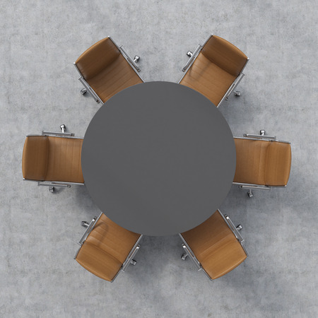 Top view of a conference room. A dark grey round table and six brown leather chairs around.