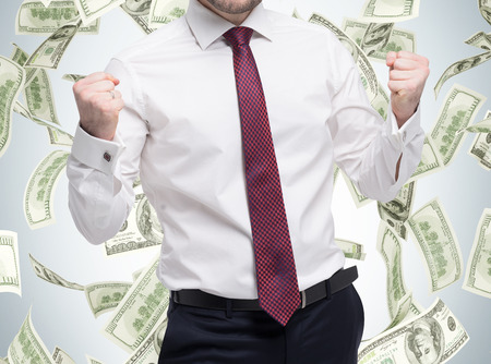 Closeup portrait of happy successful student, business man who has reached the goal. Fists pumped. The concept of celebrating the success. Dollar note are falling down over the isolated background.の写真素材