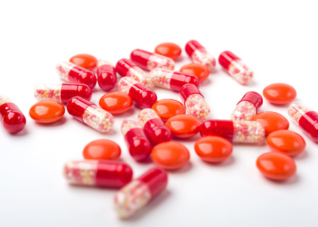 Spilled red medicine pills and capsules on white surface.