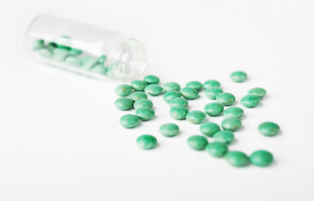 Green spilled Pills from a bottle on white surfaceの写真素材