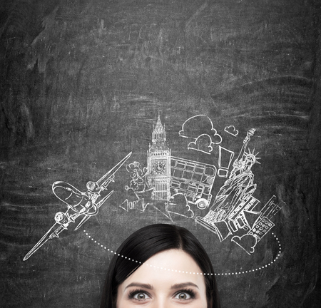 Forehead of brunette lady who thinks about travelling. New York and London sketches are on the black chalkboard. The concept of anticipation of the adventure.の写真素材