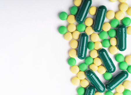 A top view of a heap of yellow and green medicine pills and capsules on white surface.の写真素材
