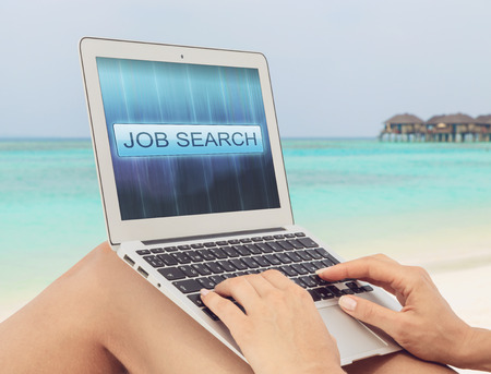Woman on the tropical beach is looking for a job using a laptop. Internet Job Search concept on the laptop's screen. Freelance as a mainstream.の写真素材