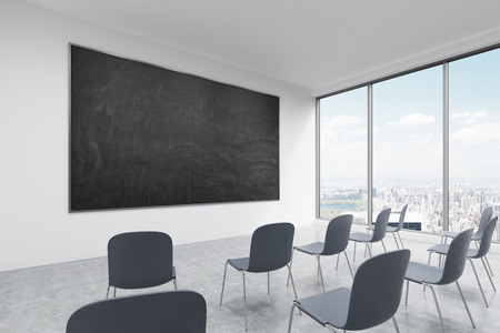 A classroom or presentation room in a modern university of fancy office. Black chairs, panoramic windows with New York view and a black chalkboard on the wall. 3D rendering.の写真素材