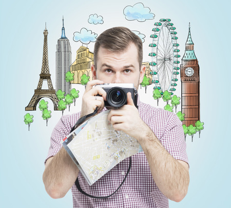 A front view of the handsome tourist with camera. Drawn sketches of the most famous touristic places on the light blue background. The concept of tourism and sightseeing.の写真素材