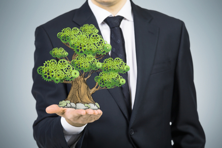 A person in formal suit holds a sketched tree on the palm. Light grey background. A concept of the business development.の写真素材