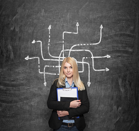 a young girl standing at a wall holding note books, blackboard with labirinth at the background, a concept of choice and studyingの写真素材