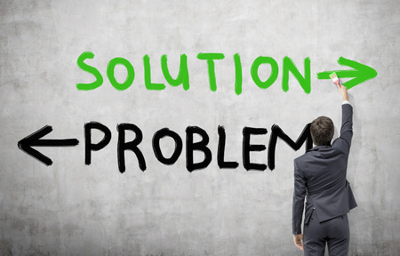 Young man painting the word 'solution' in green as contrary to 'problem in black. Concrete background. Concept of finding a solution.の写真素材