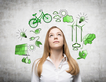 A woman looking up and dreaming, symbols of alternative energy sources painted in green colours on a white poster behind her. Concept of clean environment.の写真素材