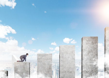 A young businessman ready to climb a career ladder in shape of a concrete bar chart, blue sky at the background. Concept of career growth.の写真素材
