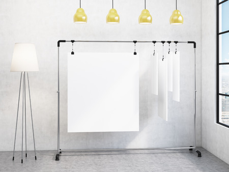 A portable rack for paper in the corner of the room, paper sheets clipped to it, window with a city view to the right, standard lamp to the left, four yellow lamps above. Concept of demonstration. 3D renderingの写真素材