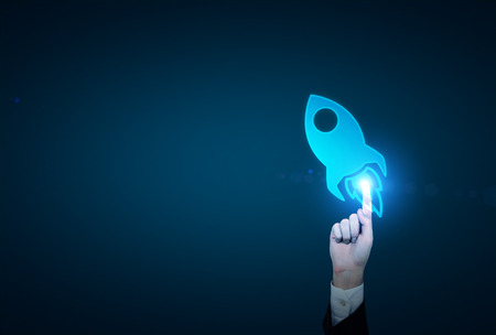 A hand touching a blue image of a rocket so that it is activated. Dark blue backgroud. Concept of...