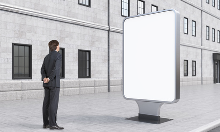 A businessman looking at a citylight in the street, city at day time. Side view. A house at the background. Concept of street advertising.の写真素材