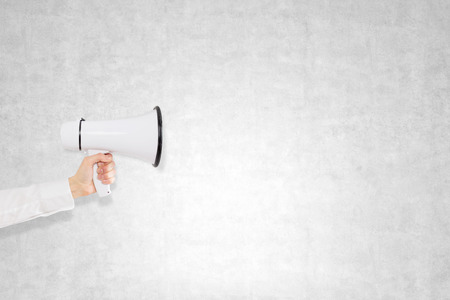 A hand holding a white loudspeaker, letters flying out from it. Side view. Concrete background. Concept of informingの写真素材