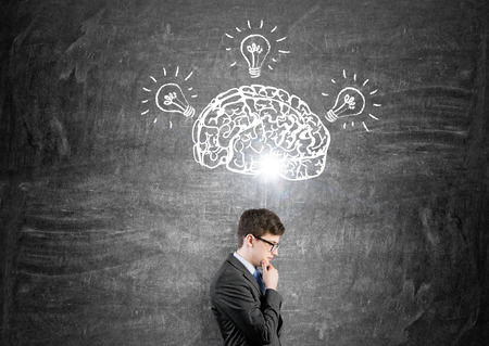 Brain and three bulbs drawn on black chalkboard. Man with hand in chin in front. Concept of mental activity.の写真素材