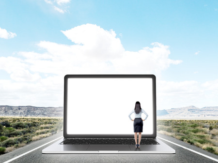Businesswoman standing on highway in front of huge laptop screen with image of New York. Blue sky at background. Back view. Concept of expectations.の写真素材