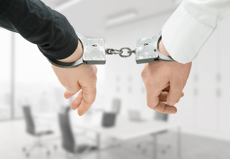 Hands of two men fixed in handcuffs. Close up. Blurred office background. Concept of accessory of...