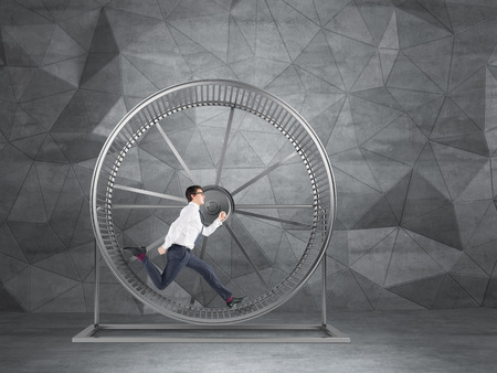 Businessman running in spinning wheel. Grey geometric background. Concept of hard work.の写真素材