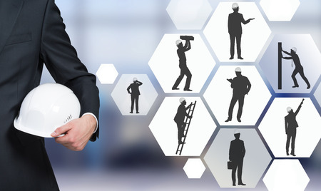 Businessman with white helmet, silhouettes of businessmen with different construction tasks near him, Blurred office background. Concept of business construction.の写真素材