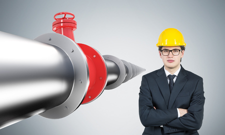 Businessman standing at metal pipe with red tap, perspective view. Grey background. Concept of pipeline.の写真素材