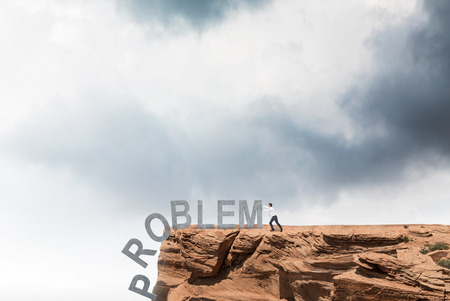 Businessman pushing letters of word 'problem' from rock. Cloudy sky at background. Concept of coping with problem.の写真素材