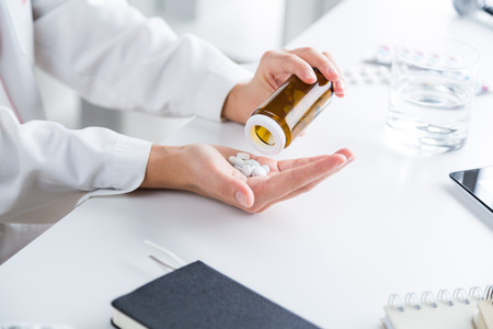 Doctor putting pills from box to her palm, only hands seen. Glass of water on table. Office. Concept of work.の写真素材