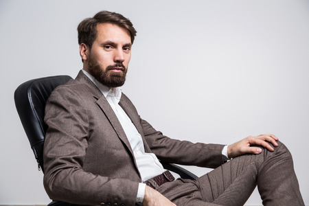 Bearded man sittin on black chair isolated on white background. Sideview, Mock upの写真素材